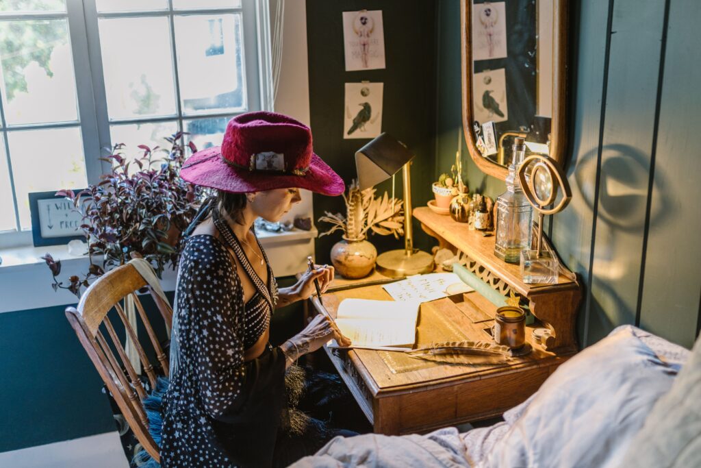 person writing in a journal at a desk with a cozy and creative workspace