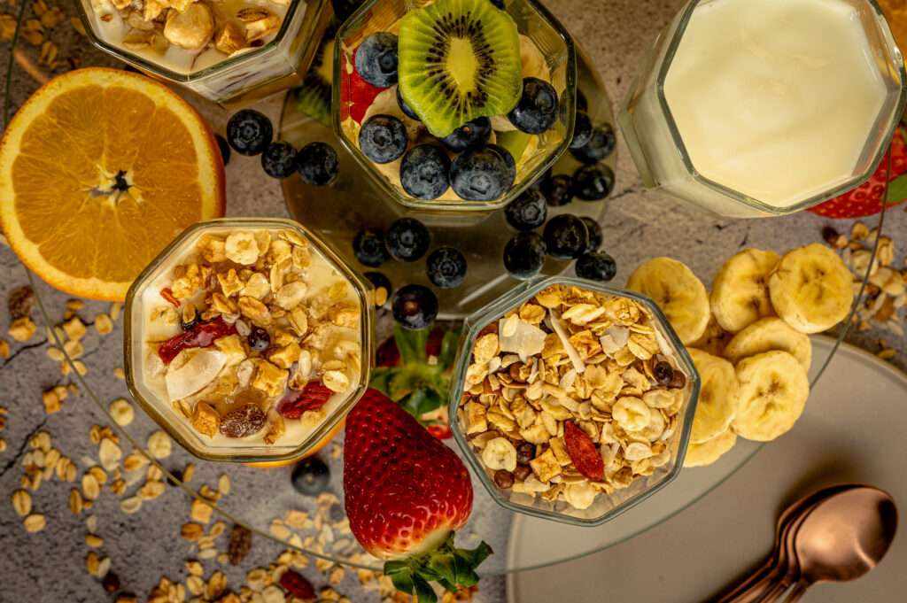 Healthy breakfast bowls topped with yogurt, granola, blueberries, kiwi, strawberries, and bananas arranged on a table.