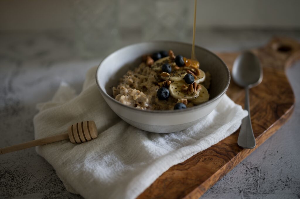 Bowl of oatmeal topped with banana slices, blueberries, nuts, and honey for a healthy breakfast.